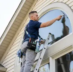 Professional window cleaner on a ladder using a squeegee to clean an exterior arched window, Cleveland, OH.